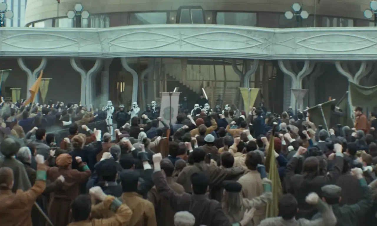 Un gruppo di manifestanti con i pugni alzati protesta verso gli Storm Trooper, l'ambientazione è quella della serie Tv Andor, nell'universo di Star Wars.