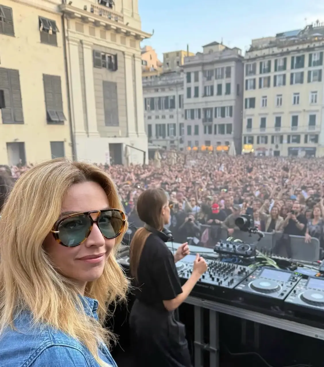 La sindaca di Genova, Silvia Salis, ritratta frontalmente con alle spalle la Dj, Charlotte De Witte, durante un evento a Genova in piazza. Decine di migliaia di persone ballano in piazza al dj set.